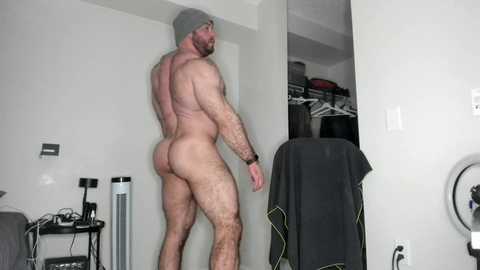 Media: Video of a muscular, naked man with a grey beanie, standing in a modern, minimalist bedroom with white walls and a closet full of clothes.