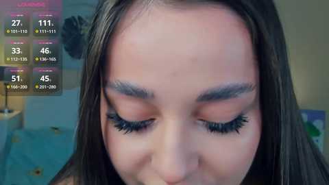 Media: Video of a young woman with long, dark hair, closed eyes, and subtle makeup, including eyeliner and mascara, in a soft, indoor setting.