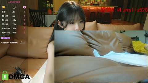 Media: A video featuring an Asian woman with long black hair, topless, lying on a brown leather couch, wearing a white towel. The background shows a modern kitchen.