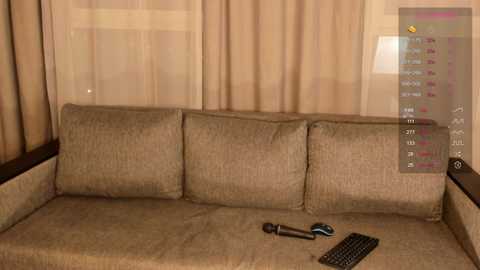 Media: Video of a beige fabric sofa with three cushions, a black keyboard, and a black mouse on a coffee table, in a room with beige curtains and a digital display showing various statistics.