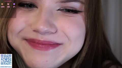 A close-up video of a young woman with fair skin, light brown hair, and a slight smile, wearing subtle makeup.