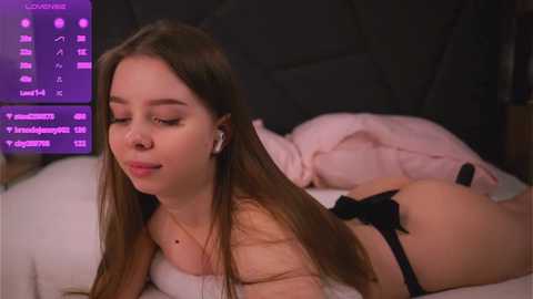 Media: Video of a young Caucasian woman with long brown hair, wearing black panties, lying on a bed, looking at a laptop displaying social media notifications.