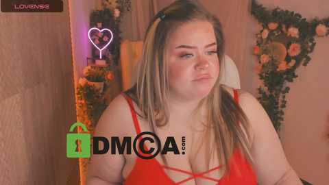 Media: Video of a plus-sized, fair-skinned woman with long blonde hair, wearing a red lace bra, pouting with a heart-shaped light in the background.