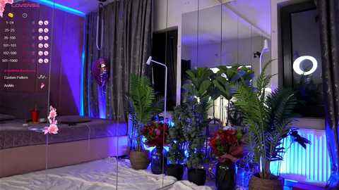 Media: Video of a modern, minimalist bedroom with mirrored walls, lush green plants, and a cozy bed, lit by blue and purple LED lights, creating a serene and stylish ambiance.