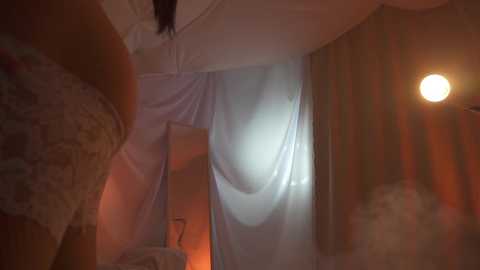 Media: Video of a dimly lit, cozy bedroom with soft, white curtains and a warm, amber lamp casting a gentle glow.