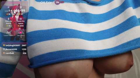 Media: Video of a woman lifting her blue and white striped sweater, exposing her large, natural breasts. Background includes a smartphone screen with chat messages and a profile picture.