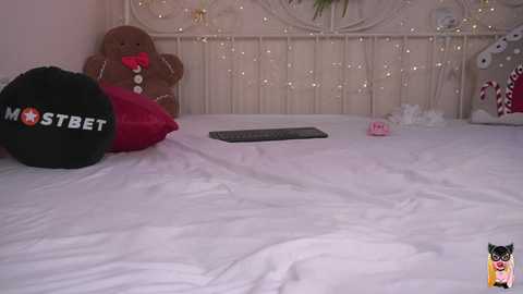 Media: Video of a cozy, white bed with a plush brown teddy bear, a black \"MOSTBET\" hat, a red pillow, and a keyboard on the mattress.