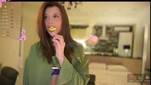 Media: Video of a young woman with long brown hair, wearing a green shirt, eating a banana in a modern, well-lit kitchen.