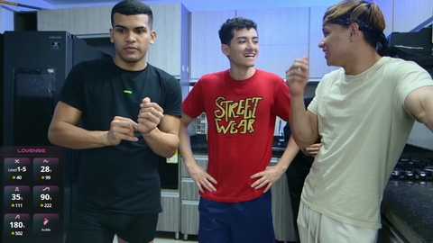 Media: Video of three young men in a kitchen, wearing casual attire. One man in black, another in red, and a third in beige. Background includes modern kitchen appliances and cabinets.