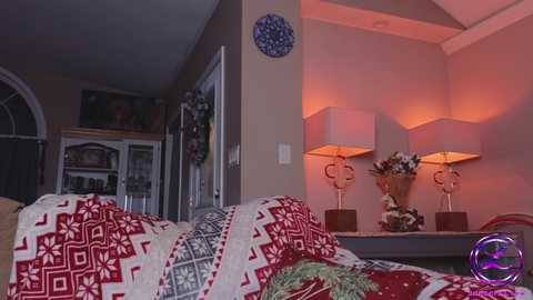 Media: Video of a cozy living room with beige walls, a red and white geometric-patterned throw on a couch, two modern lamps, a decorative vase, and a blue ceramic wall piece.