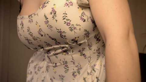 Media: Video of a light-skinned woman in a sleeveless, white floral sundress with a gathered waist, highlighting her ample bust and curvy figure. The background is blurred, focusing attention on her dress.