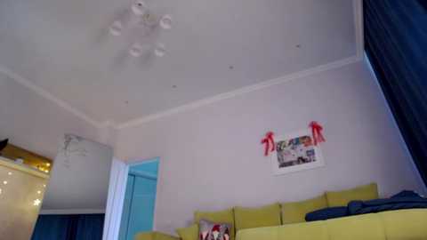 Video of a brightly lit, modern living room with a white ceiling, yellow sofa, and colorful wall decorations including a large poster and red bows.