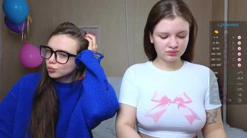 Media: Video of two young women in a room; one with long brown hair, blue sweater, and glasses; the other with short brown hair, white shirt, and pink bow.