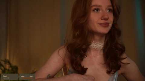 Media: Video of a fair-skinned woman with wavy, auburn hair in a satin dress, wearing a choker necklace. She's indoors, looking contemplative, with warm, dim lighting.