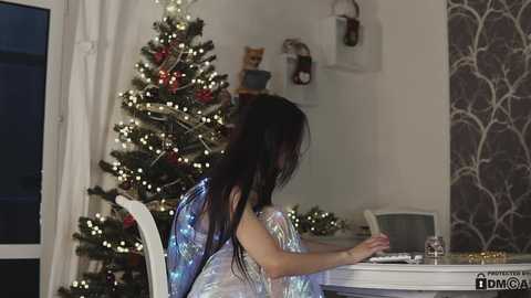 Media: A video of a woman with long, dark hair in a silver fairy costume writing at a white table, surrounded by a decorated Christmas tree and festive decor.