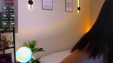 Media: A video of a cozy bedroom with a glowing white orb lamp, minimalist wall art, and a person's arm seen from the back, standing near the bed.