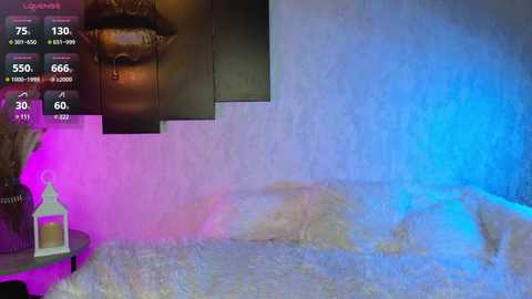 Video of a dimly lit, textured, cave-like room with blue and pink lighting. A large, distorted mouth sculpture is on the left wall, and a small table with a lamp is visible.