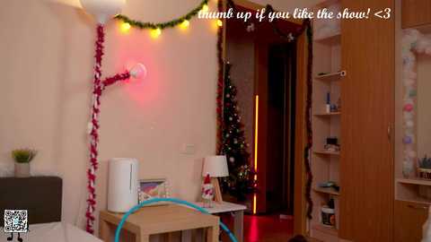 Media: Video of a cozy, Christmas-decorated bedroom with a small tree, festive lights, a white lamp, and a blue water bottle; text reads \"Mummy up if you like the show!\