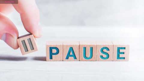 Media: Video of a light-skinned hand holding a wooden block with the letter \"P\" in turquoise, positioned above a wooden block spelling \"PAUSE\" in turquoise letters. The background is a blurred, neutral-toned wall.