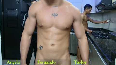 Media: Video of two naked men in a modern kitchen: one muscular with tattoos on chest and hip, the other with toned physique and short dark hair.