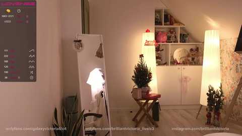 Media: Video of a cozy, modern room with white walls, a white cabinet, a small table, and a Christmas tree, illuminated by warm, ambient lighting.