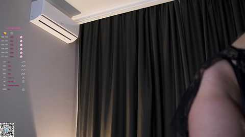 Media: Video of a modern room with a black curtain covering a window, an air conditioning unit on the left wall, and a blurred person in black clothing partially visible on the right.