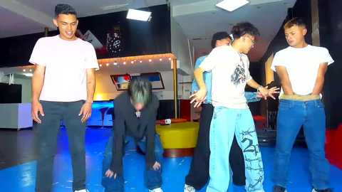 Media: Video of five young men in a brightly lit indoor space; two standing, three crouched, all wearing casual attire, smiling.