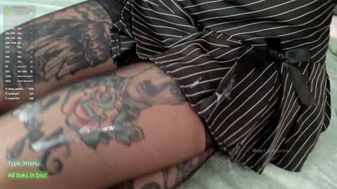 Media: Video of a person wearing black and white striped pajamas, with visible tattoos on their legs including a large rose. The background is blurred, with green text overlay.