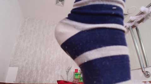 Media: A video of a person wearing navy and white striped socks standing in a room with white walls, a Christmas tree, and a red and green gift pile.