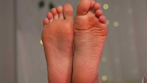 Media: Video of two bare feet with slightly wrinkled soles, toes slightly curled, against a blurred background featuring soft, glowing light orbs.