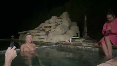 Media: A video of a dimly-lit poolside scene at night; a man with a phone, a woman with a drink, and a man in a robe, near a rock waterfall.