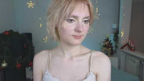 Media: Video of a pale-skinned, short-haired young woman with freckles, wearing a lacy white camisole, in a softly lit, festive living room adorned with Christmas decorations.