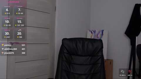 Media: Video of a modern bedroom with a black leather office chair draped with a black blanket, a white dresser, and a black coat hanging on a wall hook.