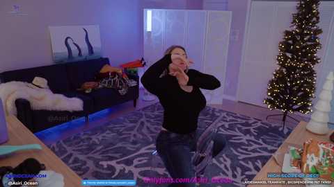 Media: Video of a woman in a black sweater and jeans, dancing in a modern living room with a dark couch, white Christmas tree, and blue carpet.