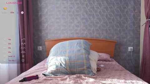 Media: Video of a cozy, neatly made bed with a light blue and pink plaid pillow, surrounded by pastel-colored curtains and a gray, geometric-patterned wall.