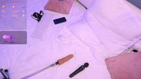 Media: Video of a white bed with a white comforter, two pillows, a silver vibrator, a black remote, and a pink vibrator on the right side. A white tablet with a pink vibrator image on the left.