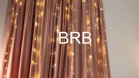 Media: Video of a room with a backdrop of light pink curtains adorned with warm white fairy lights. The text \"BBR\" is prominently displayed in the center. The image evokes a cozy, festive atmosphere.