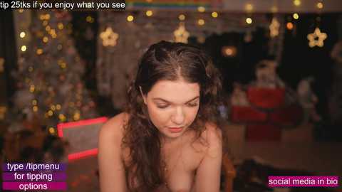 Media: Video of a young woman with long brown hair, topless, in a dimly-lit room with Christmas decorations and text overlays about social media options.