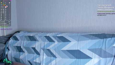 Media: Video of a bed with a geometric-patterned blue and white duvet cover in a light gray room. Text overlays mention Twitch streamer May, with chat messages visible.