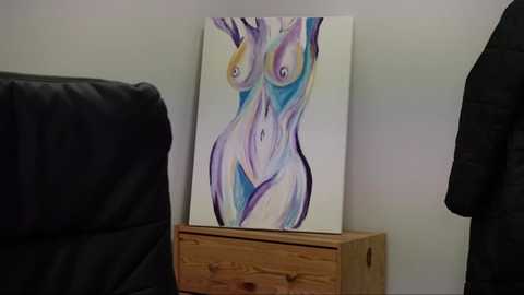 Media: Video of a colorful abstract painting on a white wall, depicting a stylized female figure with large, expressive eyes, set against a light wooden dresser and black leather couch in a modern living room.