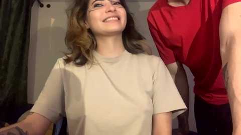 Media: Video of a smiling woman with shoulder-length brown hair, wearing a beige t-shirt, being styled by a person in a red t-shirt.