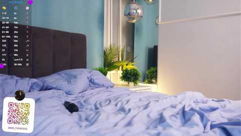 Media: Video of a neatly made bed with light blue sheets, a dark headboard, and a white nightstand with a small potted plant. The room has turquoise walls, a large mirror, and a modern light fixture.