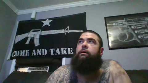 Media: A video of a bearded man in a sleeveless shirt, with a large black flag featuring a rifle and \"COME AND TAKE IT\" text. A black-and-white framed photo hangs on the wall.