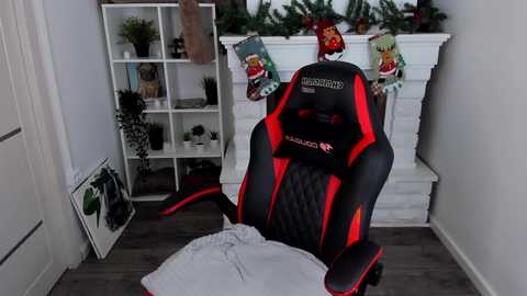 Media: Video of a modern gaming room with a black and red Corsair gaming chair, a white bookshelf, green plants, a white fireplace, and Christmas decorations.