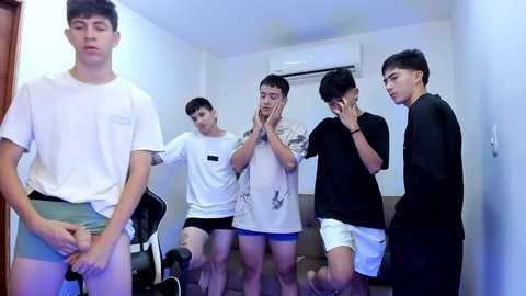 Media: Video of four Asian teenage boys in casual T-shirts and shorts, startled by a man in a white shirt, standing in a simple, white-walled room.