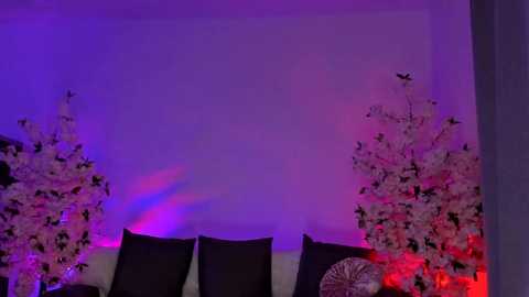 Media: A video of a dimly lit room with purple and red lighting, featuring a white tree with black butterflies and a black fan on a white couch.