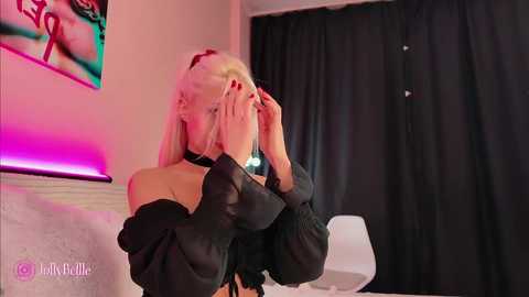 Media: Video of a blonde woman in a black off-shoulder top, adjusting her hair, with neon lights in the background.