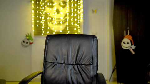 Media: Video of a black leather office chair with a backlit yellow skull wall art and two paper m\u00e2ch\u00e9 masks hanging on the wall.