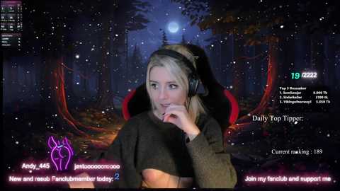 Media: A video of a blonde woman with headphones, wearing a black top, sitting in a dimly lit, forested room with a full moon. Text overlay reads \"Join my stream\" and \"Amy 498.\