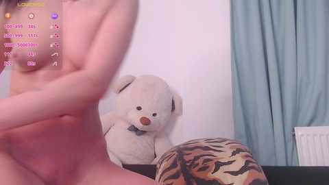 Media: Video of a nude woman with small breasts and light skin, standing in a room with a stuffed tiger and white teddy bear.